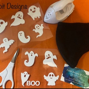 May include: A set of white iron-on ghost designs for Halloween crafts. The designs include various ghost shapes and the word "BOO". A black face mask, a small iron, and scissors are also pictured.