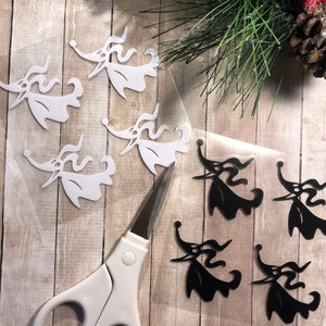 May include: A sheet of white vinyl with four black and white Jack Skellington cutouts. The cutouts are in the shape of Jack Skellington's head and shoulders. The cutouts are on a wooden surface.