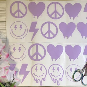 May include: A sheet of purple vinyl stickers with various designs, including peace signs, hearts, lightning bolts, and smiley faces. The stickers are arranged in rows on a white background.