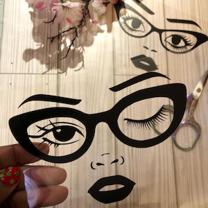 May include: A black and white silhouette of a woman's face with glasses and a closed eye. The woman is wearing thick-framed glasses with a cat-eye shape. The woman's lips are closed and her nose is small.