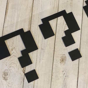 May include: Two black pixelated question marks on a light wood background.