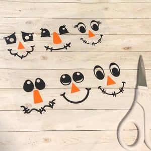 May include: Five different black and orange felt cutouts of cartoon faces with various expressions. The faces are on a white background.