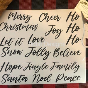 May include: A white sheet of paper with black text. The text includes Christmas greetings such as "Merry Christmas", "Let it Snow", "Hope", "Fingle", "Family", "Santa", "Noel", "Peace", "Cheer", "Joy", "Ho", "Love", "Folly", "Believe".