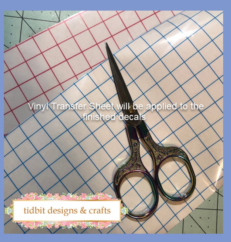 May include: A clear vinyl transfer sheet with a blue grid pattern. A pair of rainbow-coloured scissors is on top of the sheet. The text "Vinyl Transfer Sheet will be applied to the finished decals" is visible on the sheet. The text "tidbits designs & crafts" is visible in the bottom left corner of the image.