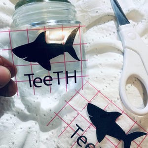 May include: A clear glass jar with a black shark silhouette and the word "TeeTH" on a white transfer sheet.