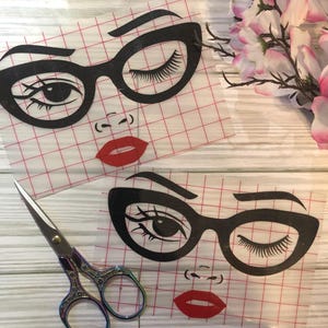 May include: Two black and white graphic designs of a woman's face with glasses and red lips on a white gridded background. The designs are on clear adhesive sheets.