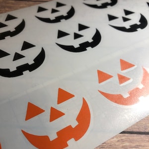 May include: A sheet of white sticker paper with black and orange jack-o'-lantern faces. The jack-o'-lantern faces are in a repeating pattern.