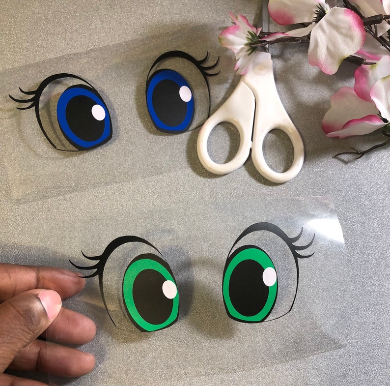 May include: Two sheets of clear vinyl with black outlines of eyes. The top sheet has two blue eyes with black pupils. The bottom sheet has two green eyes with black pupils.