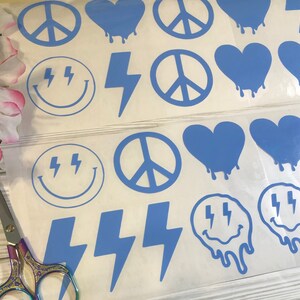 May include: A sheet of blue vinyl stickers with various designs, including peace signs, hearts, lightning bolts, and smiley faces. The stickers are perfect for adding a pop of color and personality to laptops, water bottles, notebooks, and more.