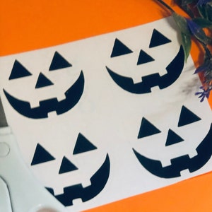 May include: Four black pumpkin face stencils on a white sheet of paper. The stencils are ready to be cut out with a pair of scissors.