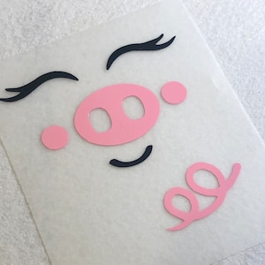 May include: Pink pig face with eyelashes, a snout, and a curly tail. The pig face is on a white background.