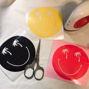 May include: Three iron-on vinyl stickers with a smiley face design. The stickers are yellow, black, and pink. Each sticker features a smiley face with two palm trees for eyes.