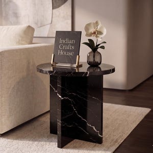 Könnte beinhalten: Ein Beistelltisch aus schwarzem Marmor mit weißen Adern, auf dem ein Schild mit der Aufschrift "Indian Crafts House" steht. Eine kleine Glasvase mit einer Orchidee steht auf dem Tisch. Der Tisch hat eine runde Platte und ein geometrisches Gestell.
