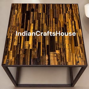 Op de afbeelding: Een vierkante salontafel met een zwart metalen frame en een blad van tijgeroog-steen. De steen is een mozaïek van bruine, gouden en zwarte stukken. De tafel is gelabeld met "IndianCraftsHouse".