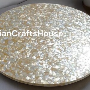 Op de afbeelding: Ronde witte en gouden parelmoer tafelblad. Het tafelblad is gemaakt van kleine, onregelmatige stukjes parelmoer die in hars zijn gegoten.