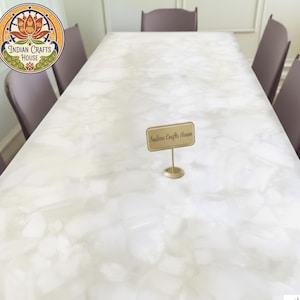 May include: A large, rectangular white table with a patterned surface, surrounded by six purple chairs. A small gold sign that reads "Indian Crafts House" is on the table. The Indian Crafts House logo is in the upper left corner.