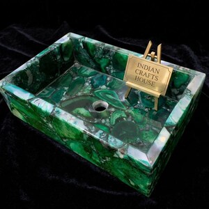 Puede incluir: Lavabo rectangular de piedra verde con acabado pulido. El lavabo presenta un patrón de mosaico de piedras verdes y blancas. Un pequeño letrero dorado que dice "INDIAN CRAFTS HOUSE" está sobre un pequeño caballete.