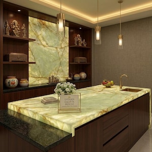 May include: A modern kitchen with a large island featuring a glowing, light green countertop. Dark wood cabinets and shelves display decorative items and statues. The wall behind the countertop has a green marble design. The sign says "INDIAN CRAFTS HOUSE".