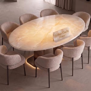 May include: An oval dining table with a translucent, backlit honey-colored onyx stone top and a dark fluted pedestal base, surrounded by eight beige upholstered chairs with dark legs. A small rectangular sign reads Indian Crafts House.