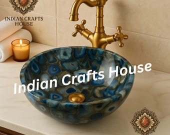 May include: A blue and gold stone vessel sink with a brass faucet. The sink has a unique pattern and is set on a white countertop. The image also includes a lit candle and a stack of white towels.