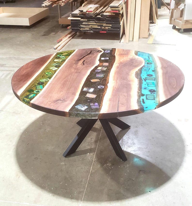May include: A round wooden table with a unique design. The tabletop features a dark brown wood grain with sections of green, black, and turquoise resin. The table is supported by a black metal base.