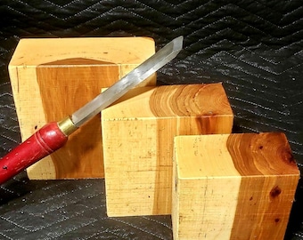 Könnte beinhalten: Ein Holzbeitel mit rotem Griff und silberner Klinge liegt auf drei Holzblöcken. Die Blöcke sind hellbraun mit dunkleren Holzmaserungen. Der Beitel ist über die Blöcke geneigt.