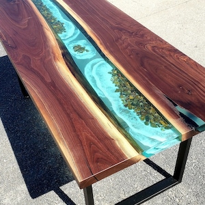 May include: A wooden table with a turquoise blue epoxy river running down the center. The river is filled with small, green stones. The table has a black metal base.