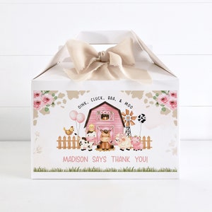 Può includere: Una scatola regalo bianca con un fienile rosa e animali della fattoria. La scatola ha un motivo a stampa di mucca marrone e bianco e un design floreale rosa e verde. Il testo sulla scatola dice "Oink. Cluck. Baa. & Moo. Madison Says Thank You!"