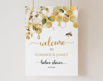 Op de afbeelding: Welkom bord voor de babyshower van Summer & James met een witte achtergrond en een gouden honingraatpatroon met druppelende honing en witte bloemen. De tekst luidt "Welkom op de babyshower van Summer & James 07.25.XX".