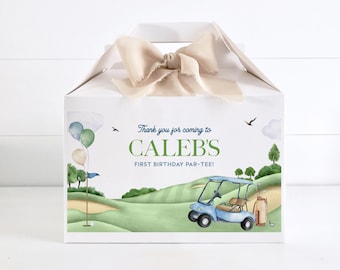 Könnte beinhalten: Weiße Geschenkbox mit einem beigefarbenen Band. Die Box hat ein Golf-Design mit einem Golfwagen, Golfschlägern und Ballons. Der Text auf der Box lautet "Vielen Dank, dass Sie zu Calebs erstem Geburtstags-Par-Tee gekommen sind!"