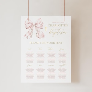 Può includere: Un piano di posti a sedere per il battesimo rosa e oro con un grande fiocco rosa e una croce. Il piano di posti a sedere elenca i nomi degli ospiti per ogni numero di tavolo, da uno a otto. Il testo recita "Battesimo di Charlotte" e "Per favore, trova il tuo posto".