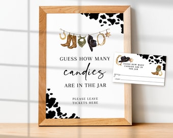Op de afbeelding: Een afdrukbaar bord voor een feestje, met een zwart-witte koe-print achtergrond. Het bord zegt "Raad hoeveel snoepjes er in de pot zitten." Er zijn illustraties van cowboylaarzen, hoeden en een hoefijzer die aan een touwtje hangen.
