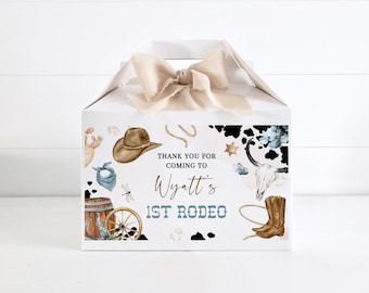 May include: White favor box with a brown cowboy hat, blue bandana, a barrel, a wagon wheel, a skull, a cowboy boot, and a lasso. The box has the text "Thank you for coming to Wyatt's 1st Rodeo".