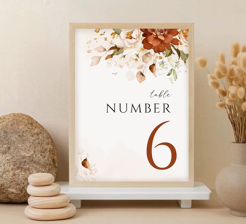 May include: A white table number card with a floral design in shades of brown, orange, and white. The text "table number 6" is printed in brown.