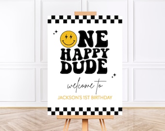 May include: A white welcome sign with black checkered borders. The sign features a yellow smiley face with lightning bolts for eyes and the text "One Happy Dude" in black retro font. The text "Welcome to Jackson's 1st Birthday" is also included in black.