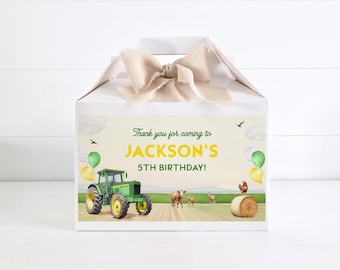 May include: White gift box with a beige ribbon bow. The box features a farm scene with a green tractor, cows, and a rooster. Text reads "Thank you for coming to JACKSON'S 5TH BIRTHDAY!" with green and yellow balloons.