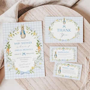 May include: A baby shower invitation set featuring a Peter Rabbit illustration, floral wreath, and blue bow accents. The invitation includes event details on a light blue gingham background. Includes thank you, diaper raffle, and books for baby cards.