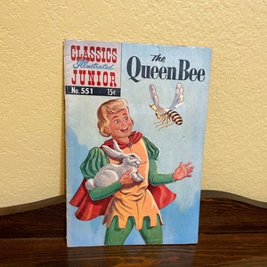 May include: A vintage illustrated children's book titled "The Queen Bee" from the Classics Illustrated Junior series. The cover features a young boy in a green and red tunic holding a white rabbit, with a bee flying above him. The book is numbered 551 and priced at 15 cents.