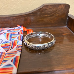 May include: A silver bangle bracelet with an intricate floral design. The bracelet is open and has a hinged clasp.