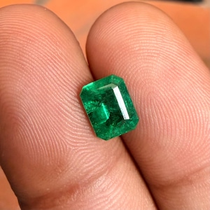Op de afbeelding: Een losse edelsteen in smaragdgeslepen vorm met een levendige, diepgroene kleur en zichtbare interne insluitingen. De steen heeft een rechthoekige vorm met gefacetteerde randen die het licht vangen en een doorschijnend, gepolijst oppervlak.