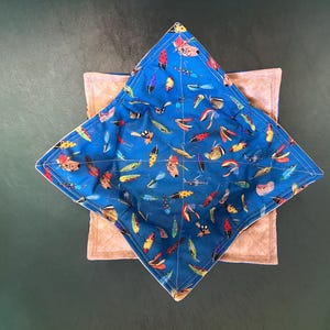 May include: A blue fabric bowl with a pattern of colorful fishing lures. The bowl is lined with a beige fabric and has a star shape.