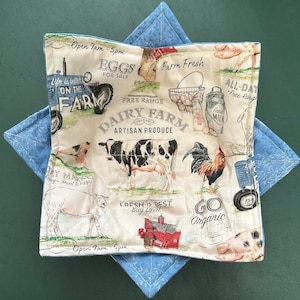 May include: A white cotton pot holder with a farmhouse theme. It features a cow, rooster, and a tractor with the text "Free Range Dairy Farm Artisan Produce" and "Go Organic".