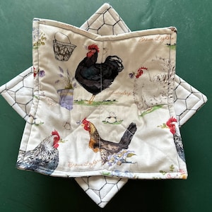 May include: A white pot holder with a chicken and egg design. The pot holder features a brown and white chicken, a basket of eggs, and the text "Brown Leghorn".