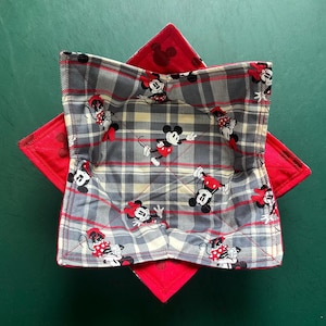 May include: A handmade bowl cozy featuring a gray plaid pattern with Mickey Mouse and Minnie Mouse designs. The cozy is reversible with a red fabric on the other side. The cozy is designed to keep food warm.