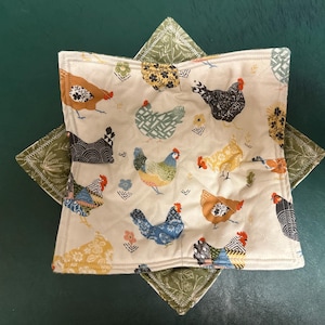 May include: A white fabric bowl with a green and white star-shaped border. The bowl is decorated with a pattern of colorful chickens and flowers.