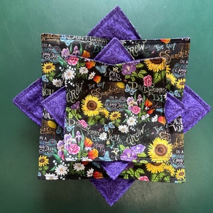May include: Four purple and black fabric pot holders with a floral and chalkboard design. The text on the pot holders reads "Don't Worry Be Happy", "I've Got Sunshine On A Cloudy Day", "You Grow Girl", and "I've Got Sunshine On A Cloudy Day".