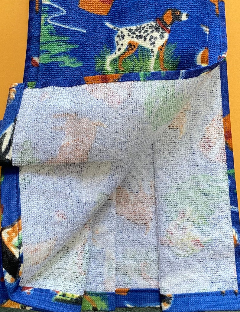 May include: A blue and white kitchen towel with a dog and camping theme. The towel is folded in half and the inside is white.