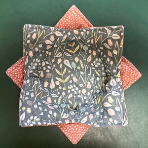 May include: A gray and pink quilted fabric bowl with a floral pattern. The bowl is made of two pieces of fabric sewn together to create a star shape.