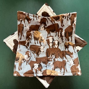 May include: A blue and white fabric bowl with a cow print design. The bowl is made of quilted fabric and has a star-shaped design.