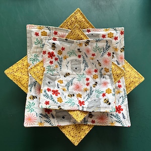 May include: Three fabric kitchen dishcloths with a honeycomb pattern and a floral pattern with bees and honeycombs. The floral pattern is repeated on all three cloths.